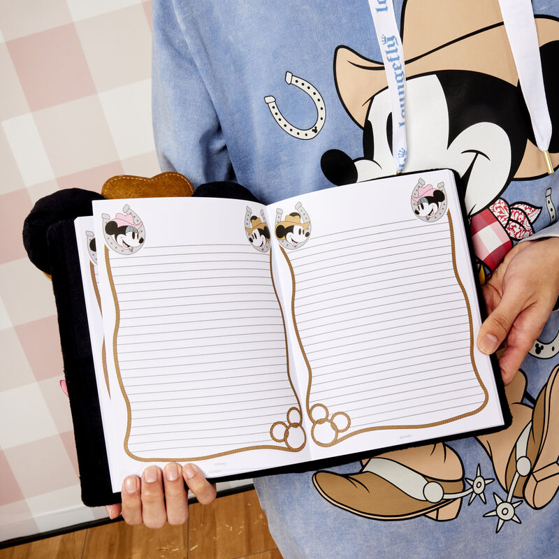 Someone wearing the blue Western Mickey Mouse hoodie and holding open the Western Mickey Mouse Plush Journals showing the lined interior pages with images of Western Mickey and Minnie and lasso details around the pages